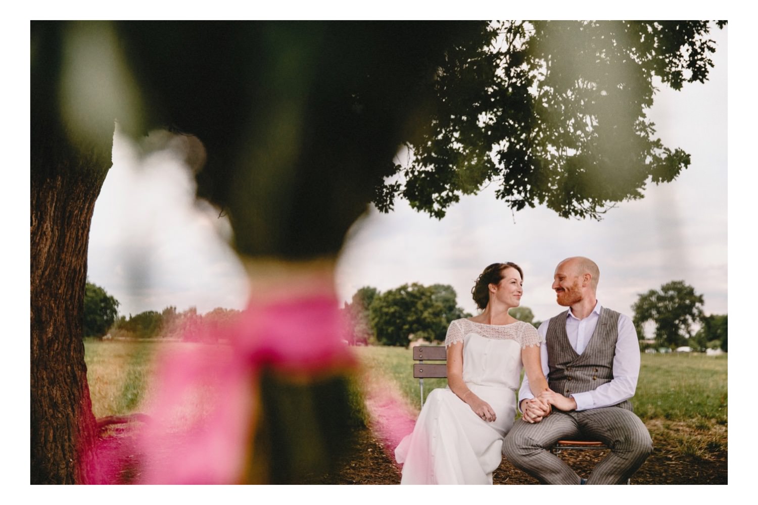 Das verliebte Brautpaar guckt sich während der freien Hochzeit in die Augen im Vordergrudn ist die Blumendeko und im Hintergrund der Hof Eggers