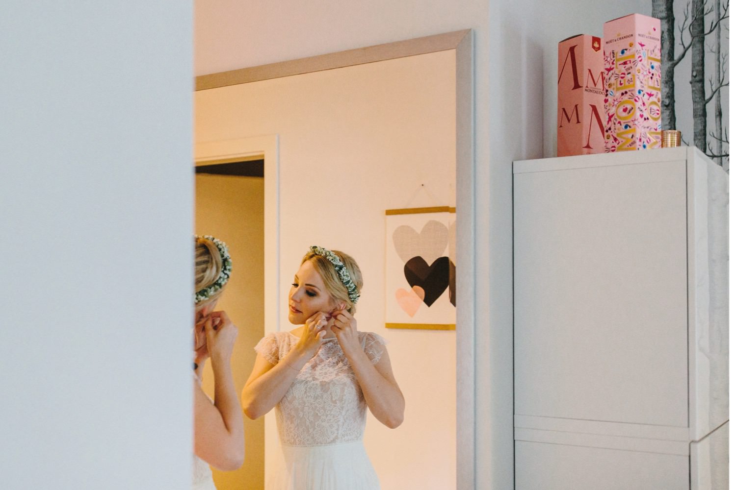 Die Braut legt sich vor einem großen Spiegel die Ohrringe an