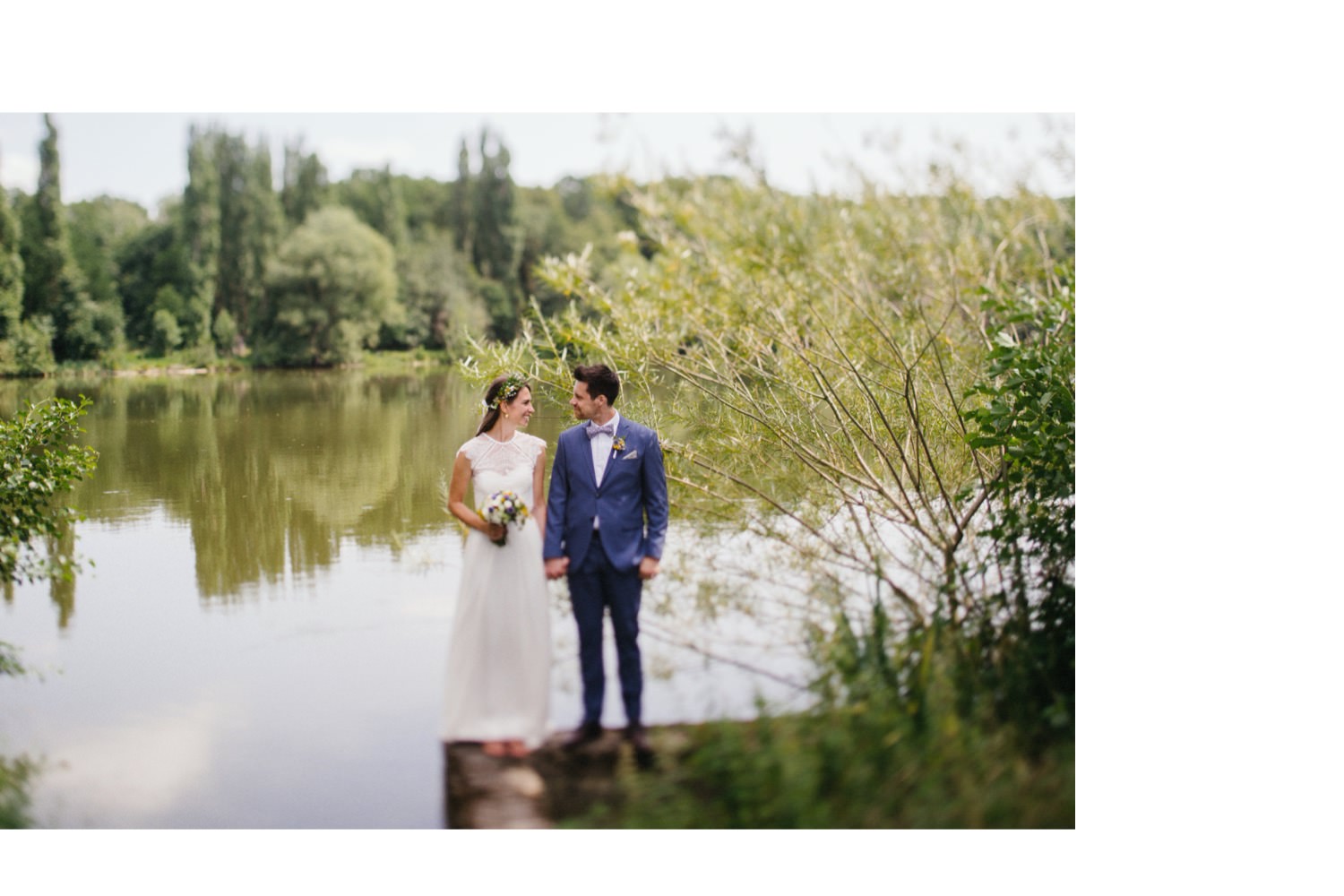 Das Hochzeitspaar steht Hand in Hand am See und guckt sich in die Augen