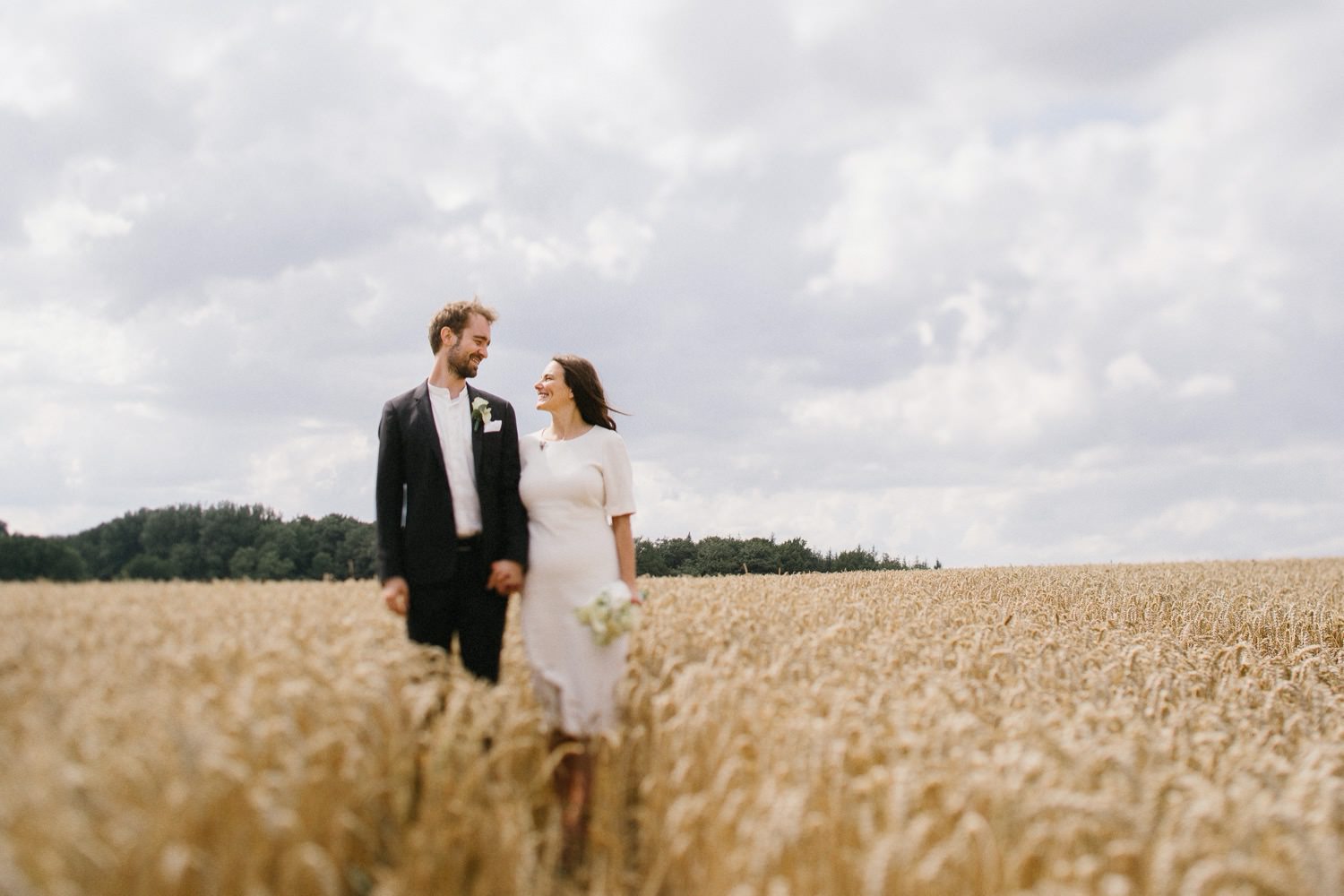 Das Brautpaar steht in einem Weizenfeld und blickt sich in die Augen an der Schlei