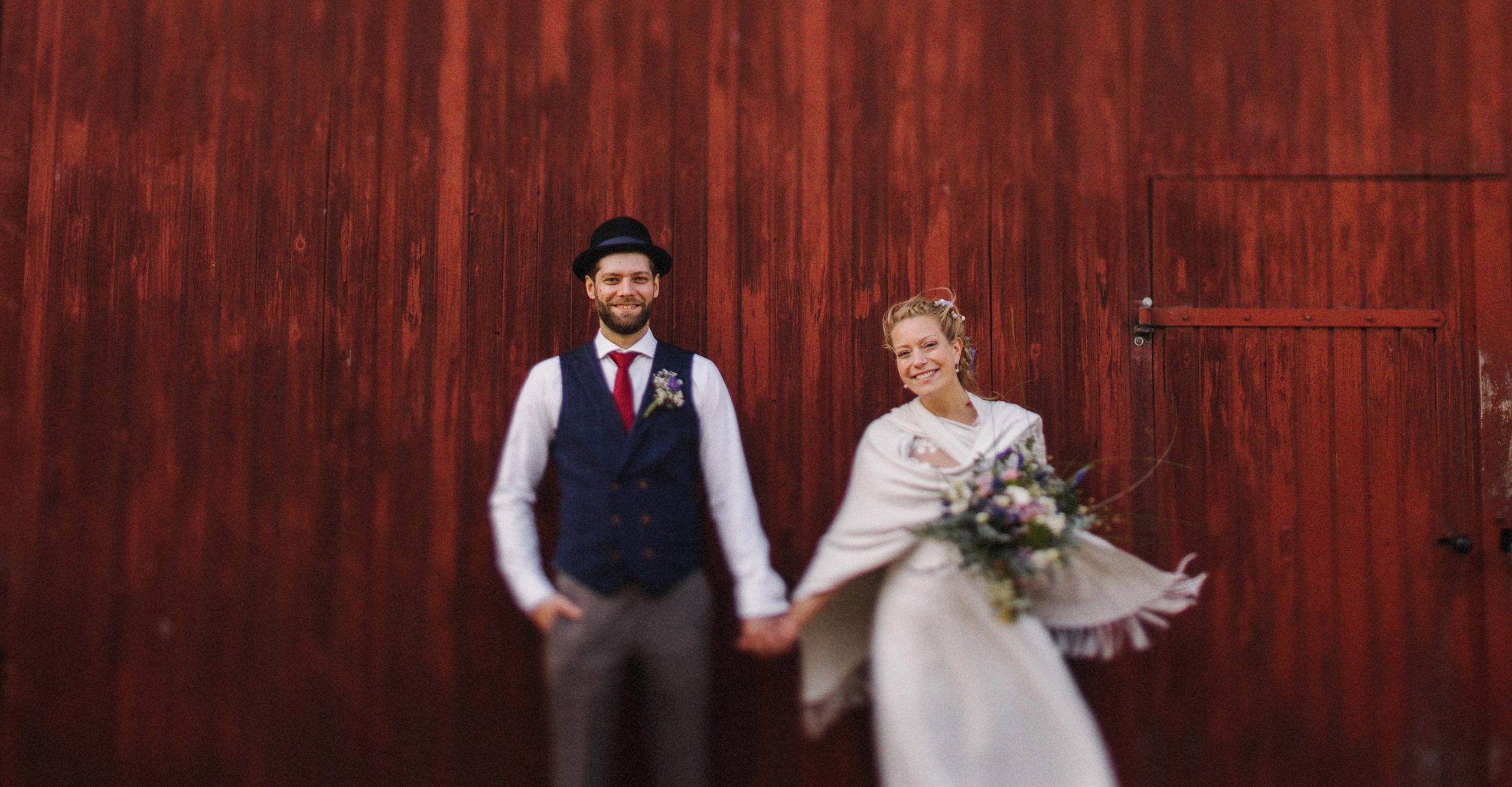 Das Brautpaar steht vor einer roten Holzwand auf dem Gut Helmstorf bei Lütjenburg