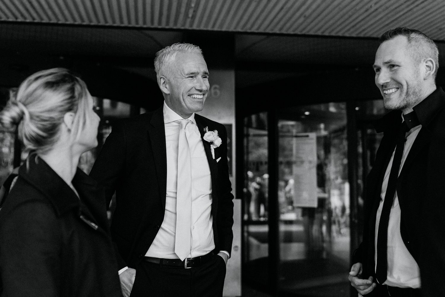 Der lachende Bräutigam steht mit seinem Bruder vor dem Eingang zum Standesamt Eimsbüttel das Foto ist schwarzweiß
