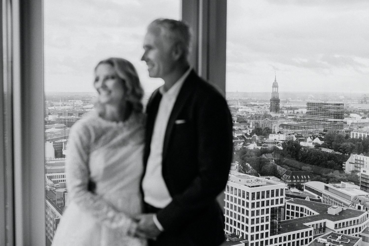 Das Brautpaar steht im Vordergrund unscharf vor den Fenstern des Panoramadeck von Nordevent im Emporiotower im Hintergrund sieht man scharf den Hamburger Michel