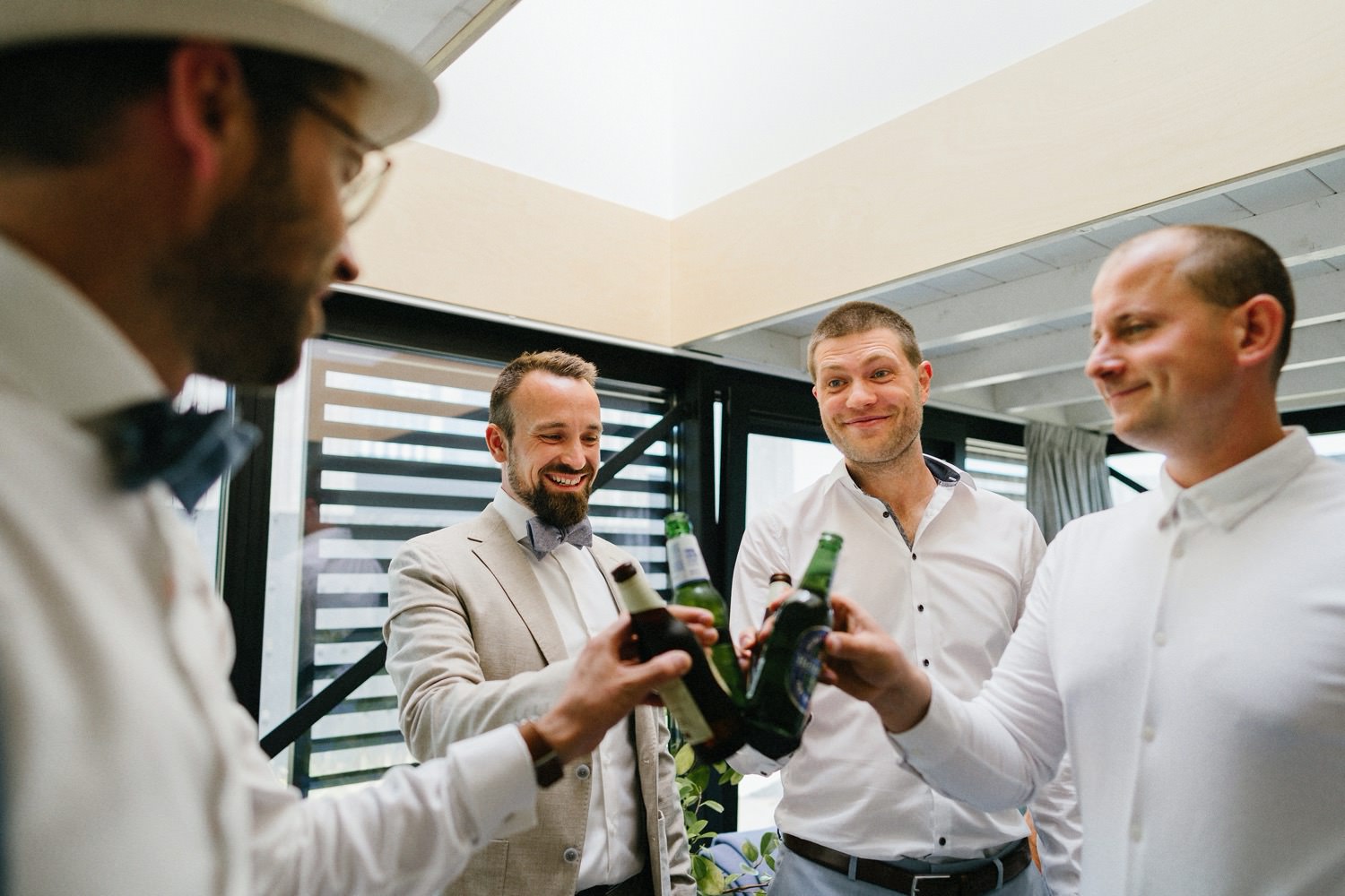 Der Bräutigam stößt voller Vorfreude im malerischen Ferienhaus in Zandvoort mit seinen besten Freunden mit Bier an. Ein intimer Moment des "Getting Ready" vor der Hochzeit, gefüllt mit Freundschaft und Vorfreude auf den besonderen Tag.