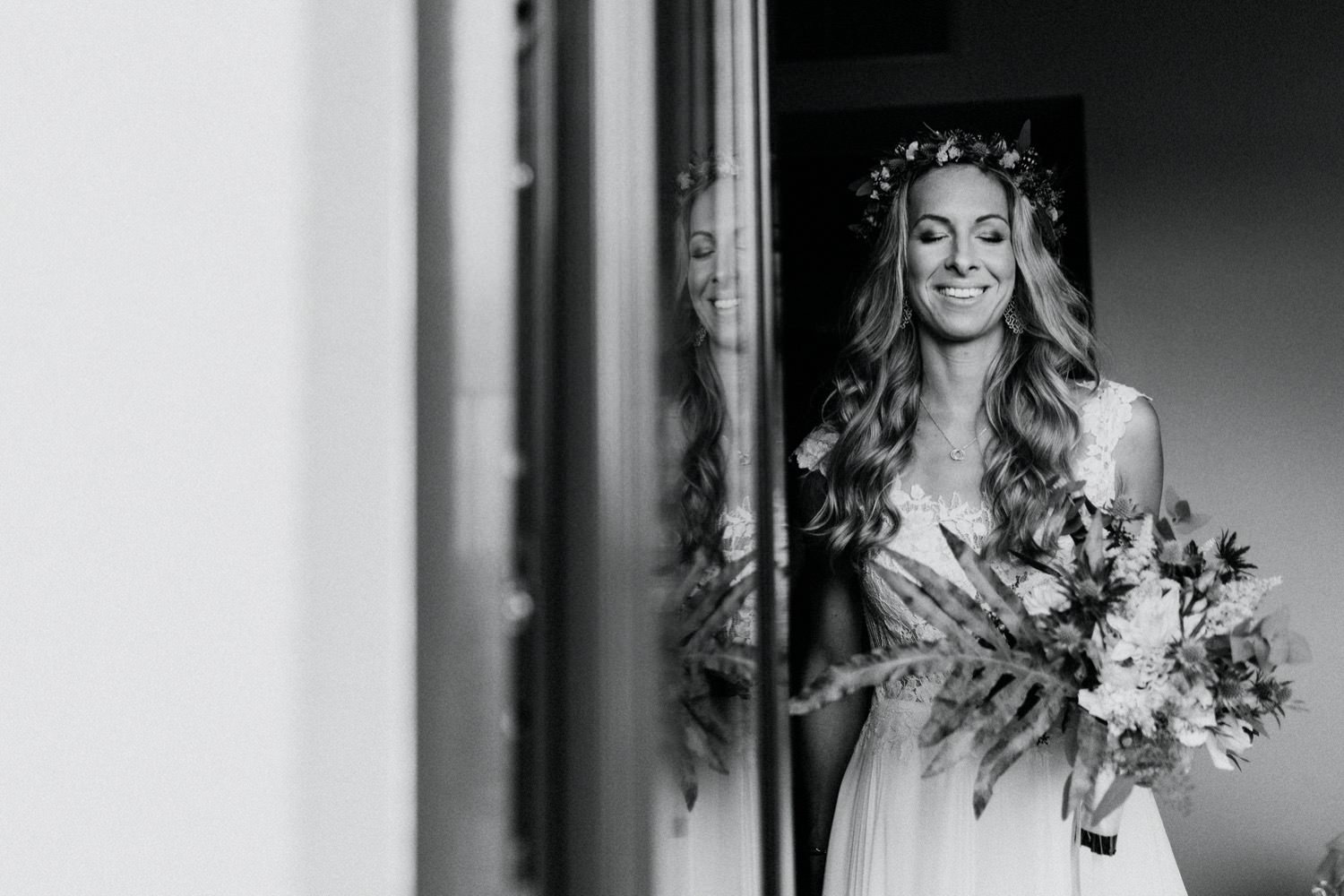 Mit geschlossenen Augen und ihrem Brautstrauß in der Hand steht die Braut vor der offenen Balkontür, um einen letzten Moment der Ruhe zu genießen, bevor sie sich auf den Weg zur Trauung begibt.