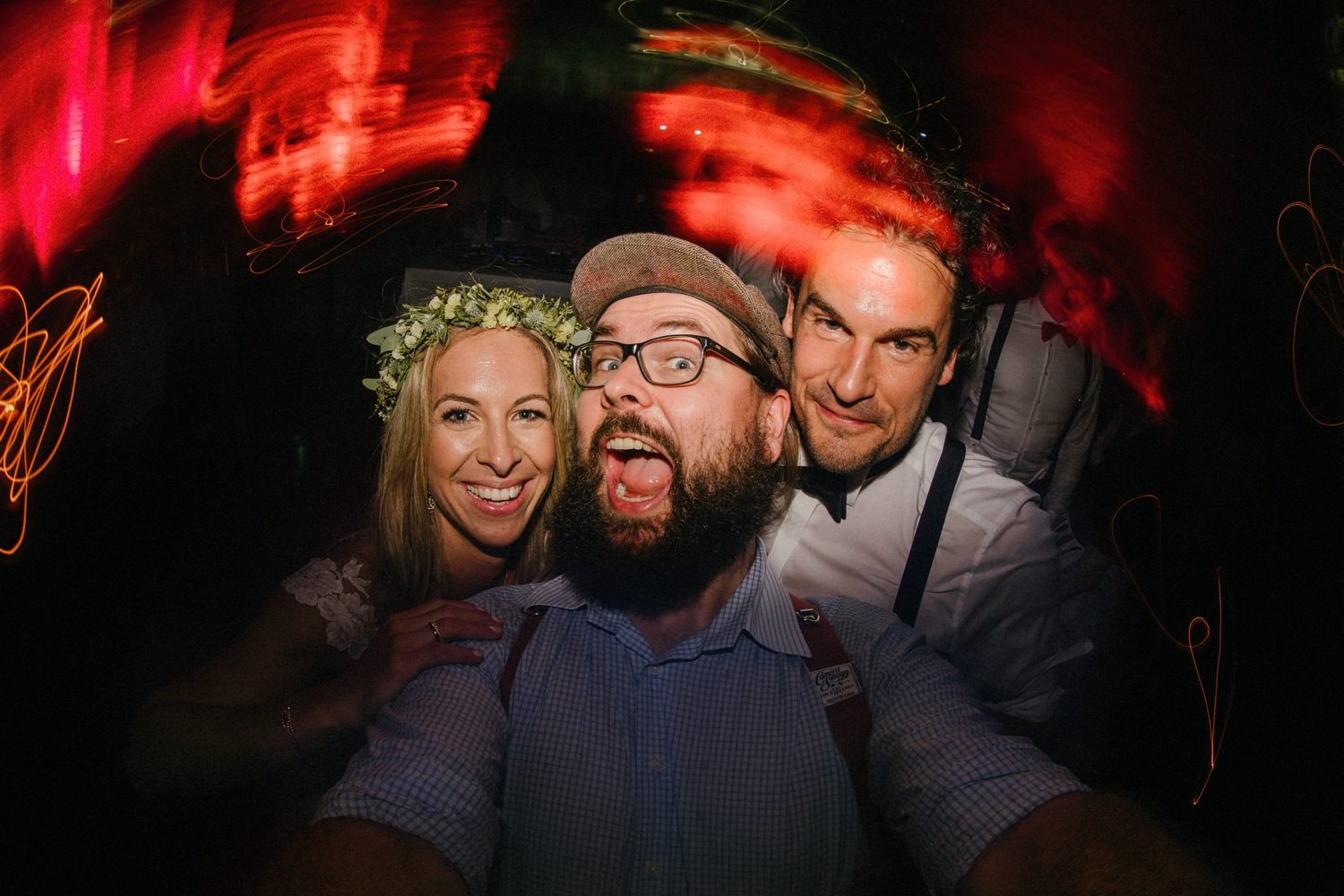 Ein Selfie des Hochzeitsfotografen Till Gläser aus Hamburg zusammen mit dem Brautpaar auf der Tanzfläche, aufgenommen mit einem Fisheye-Objektiv. Die Langzeitbelichtung erzeugt dynamische und faszinierende Lichteffekte, die die Stimmung der Feier einfangen und dem Bild eine besondere Atmosphäre verleihen.